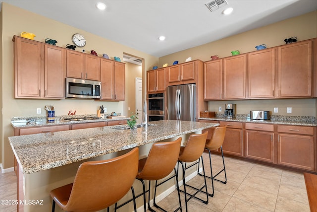 kitchen with a center island with sink, stainless steel appliances, visible vents, a sink, and a kitchen bar