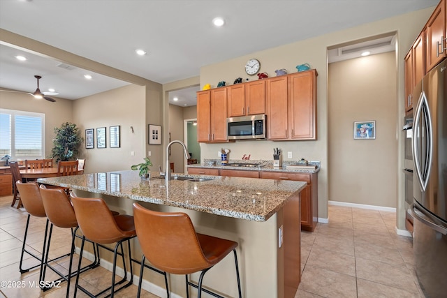 kitchen featuring light stone counters, a center island with sink, a breakfast bar area, appliances with stainless steel finishes, and a sink