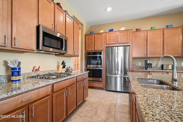 kitchen with light tile patterned floors, light stone countertops, a sink, appliances with stainless steel finishes, and brown cabinets