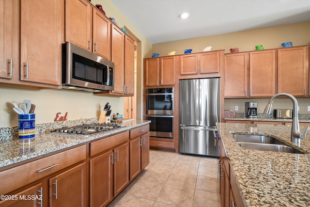 kitchen featuring stainless steel appliances, a sink, light tile patterned flooring, light stone countertops, and brown cabinetry