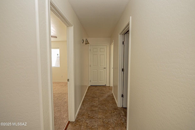 hallway featuring a textured wall, dark carpet, and baseboards