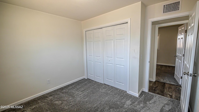 unfurnished bedroom featuring visible vents, baseboards, a closet, and dark carpet