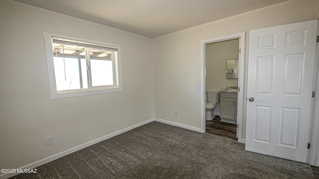 unfurnished bedroom with baseboards, dark colored carpet, and ensuite bathroom