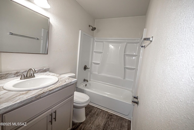 bathroom featuring toilet, wood finished floors, bathing tub / shower combination, a textured wall, and vanity