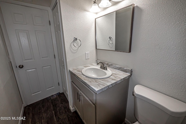 bathroom with toilet, vanity, a textured wall, and wood finished floors