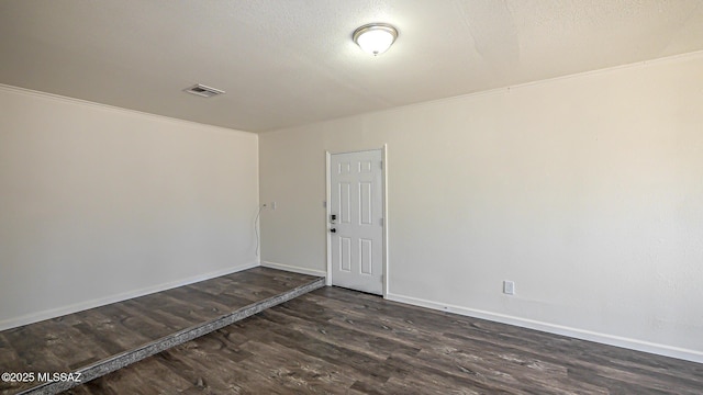 empty room featuring dark wood-type flooring, baseboards, visible vents, and a textured ceiling