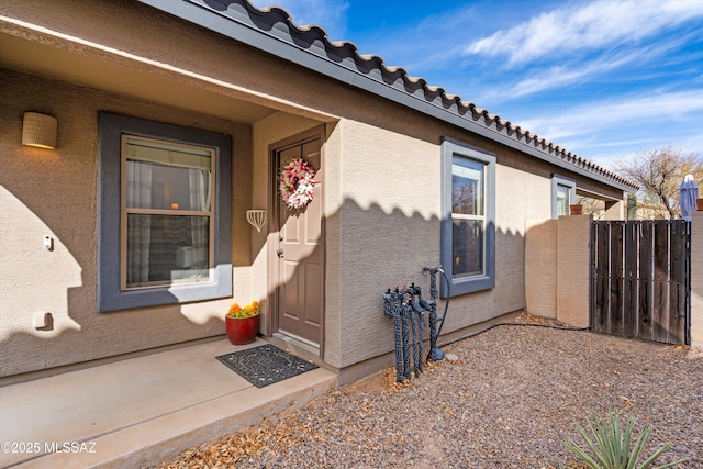 entrance to property with a tile roof, fence, and stucco siding