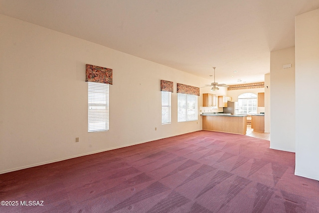 unfurnished living room with light colored carpet, ceiling fan, and baseboards