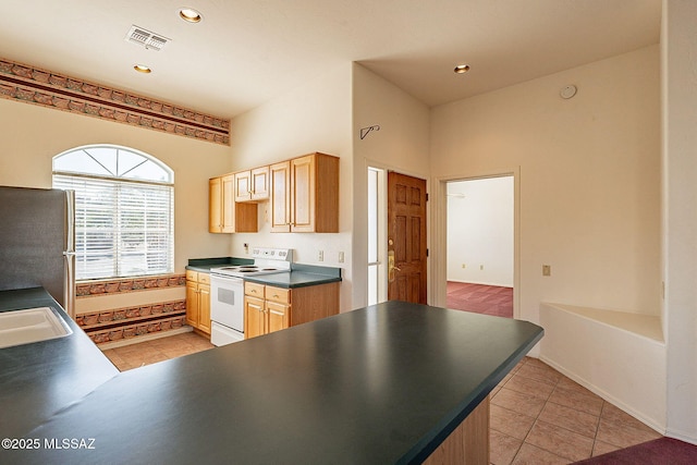 kitchen with white electric stove, light tile patterned floors, dark countertops, and freestanding refrigerator