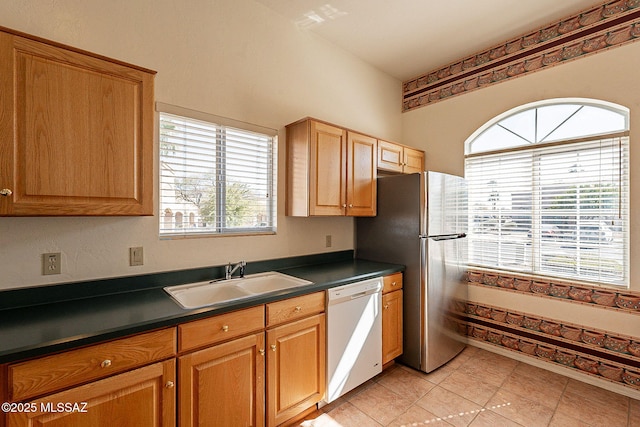 kitchen featuring dark countertops, white dishwasher, a sink, and freestanding refrigerator