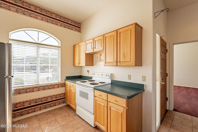 kitchen with white electric range oven, light tile patterned floors, dark countertops, freestanding refrigerator, and light brown cabinetry