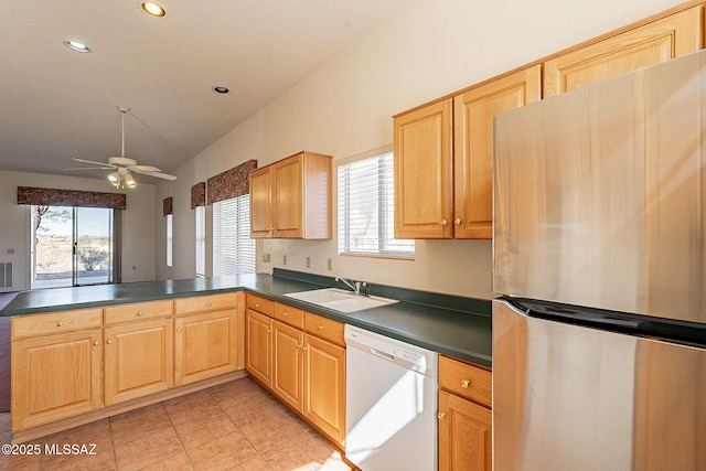 kitchen with dark countertops, freestanding refrigerator, a peninsula, white dishwasher, and a sink