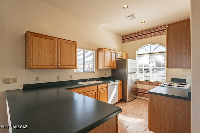 kitchen with dark countertops, white dishwasher, a sink, and freestanding refrigerator