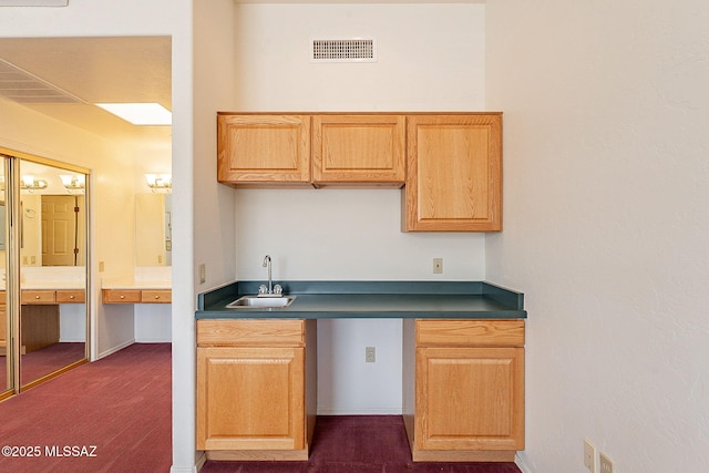 kitchen with dark colored carpet, dark countertops, a sink, and visible vents