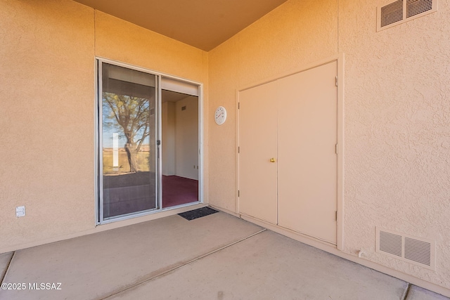 view of exterior entry featuring a patio area, visible vents, and stucco siding