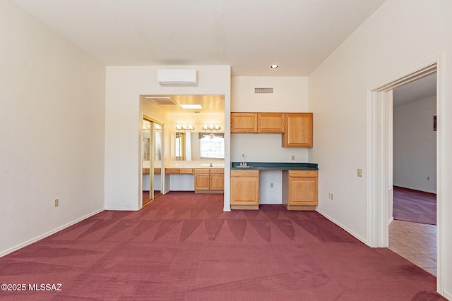 kitchen with a wall unit AC, a sink, visible vents, built in study area, and dark colored carpet