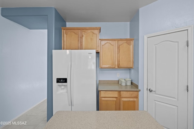 kitchen featuring light brown cabinetry, white fridge with ice dispenser, light countertops, and light tile patterned flooring