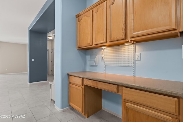 kitchen featuring baseboards, built in desk, and light tile patterned floors