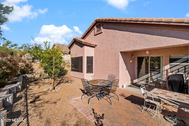 rear view of house with outdoor dining area, a patio area, a tile roof, and stucco siding