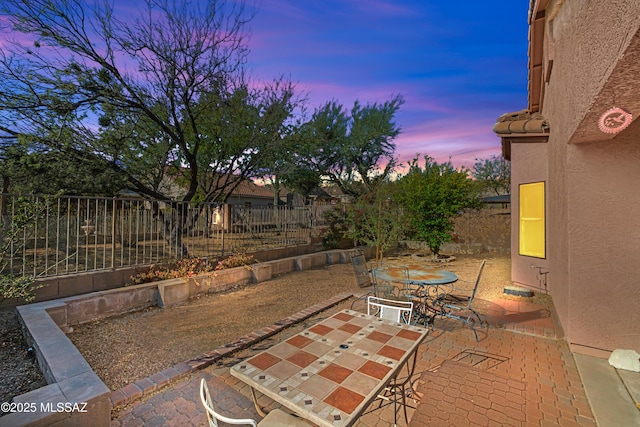 patio terrace at dusk featuring outdoor dining area and fence