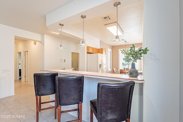 kitchen with visible vents, pendant lighting, white refrigerator with ice dispenser, a breakfast bar area, and light tile patterned floors