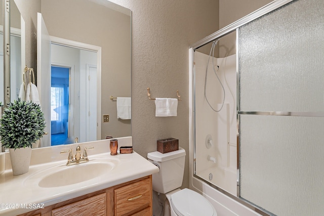 full bathroom featuring bath / shower combo with glass door, toilet, vanity, and a textured wall