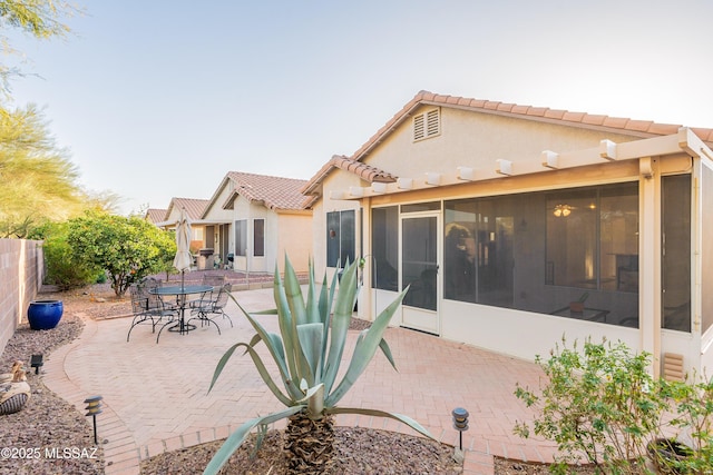 rear view of house with stucco siding, a fenced backyard, a patio area, a sunroom, and a tiled roof