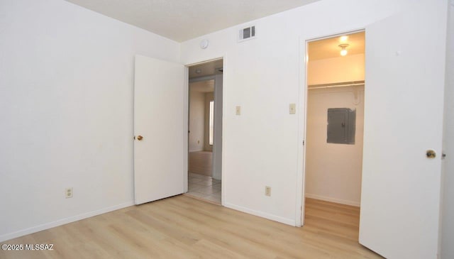 unfurnished bedroom featuring electric panel, visible vents, a walk in closet, and wood finished floors