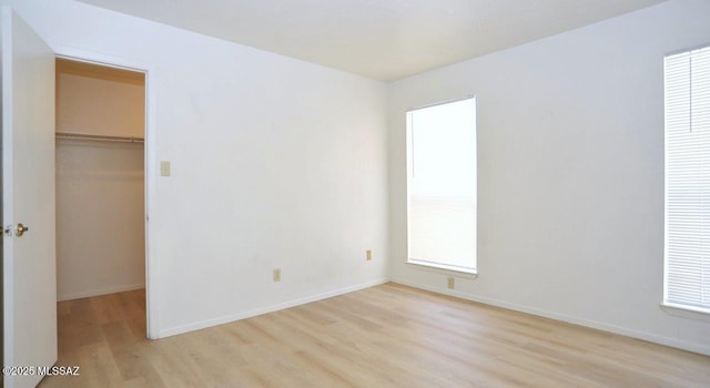 unfurnished bedroom featuring light wood-type flooring, a closet, a spacious closet, and baseboards