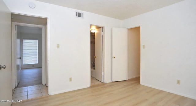 unfurnished bedroom with baseboards, visible vents, light wood finished floors, and ensuite bathroom