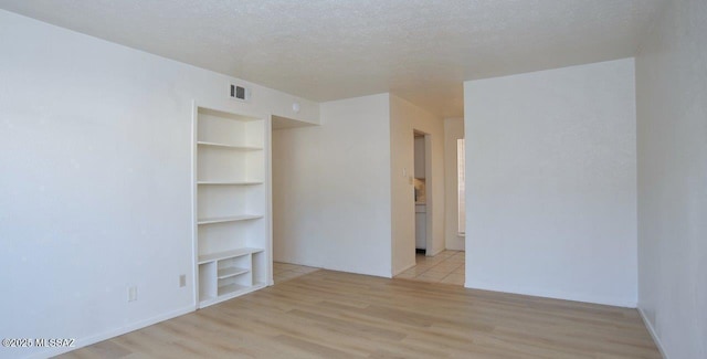 empty room with built in shelves, light wood-type flooring, visible vents, and a textured ceiling