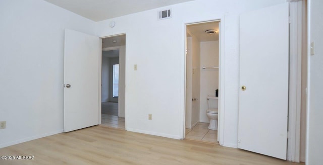 unfurnished bedroom featuring light wood-style flooring, ensuite bath, visible vents, and baseboards