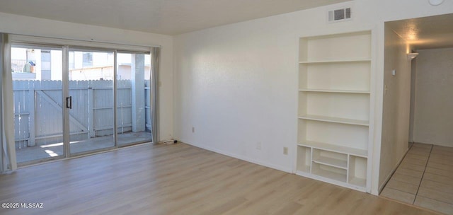 spare room with baseboards, visible vents, built in features, and wood finished floors