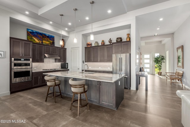 kitchen featuring dark brown cabinetry, under cabinet range hood, appliances with stainless steel finishes, and a sink