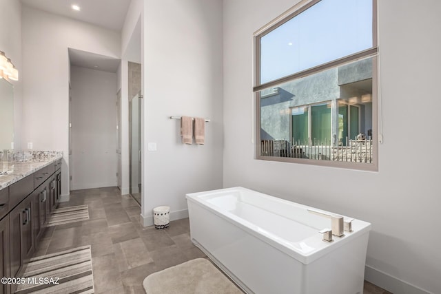 bathroom featuring a stall shower, baseboards, a bath, and vanity