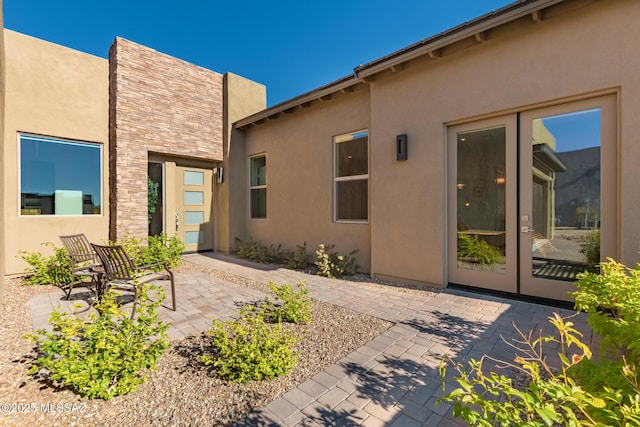 rear view of property with a patio area, stone siding, french doors, and stucco siding