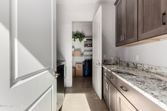 kitchen with light tile patterned floors, light stone counters, a sink, and dark brown cabinetry