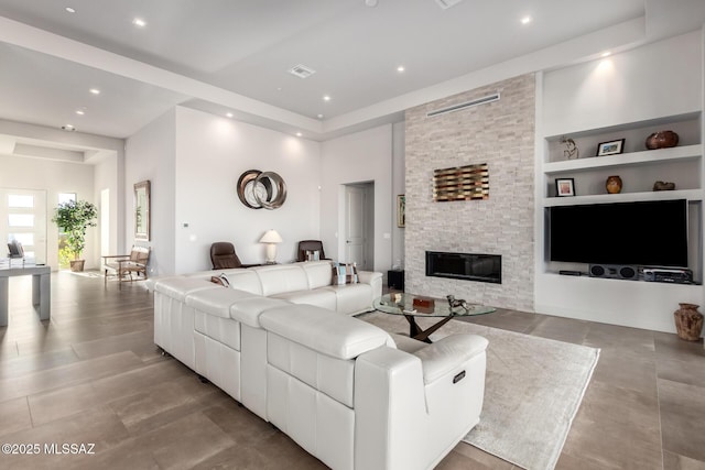 living area featuring built in shelves, recessed lighting, visible vents, and a stone fireplace