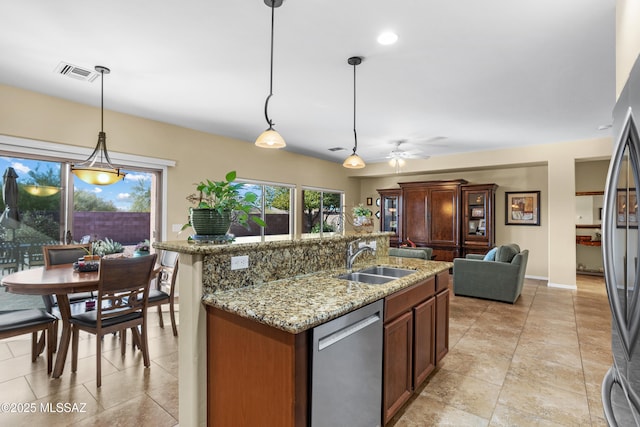 kitchen featuring light stone counters, stainless steel appliances, a sink, visible vents, and a center island with sink