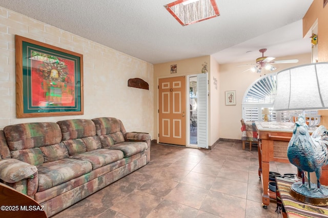 living room featuring baseboards, a ceiling fan, and a textured ceiling