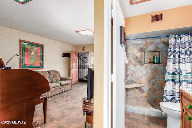 bathroom featuring toilet, visible vents, a tile shower, and a textured ceiling