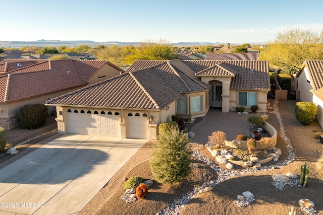 mediterranean / spanish-style home with an attached garage, driveway, a tiled roof, and stucco siding