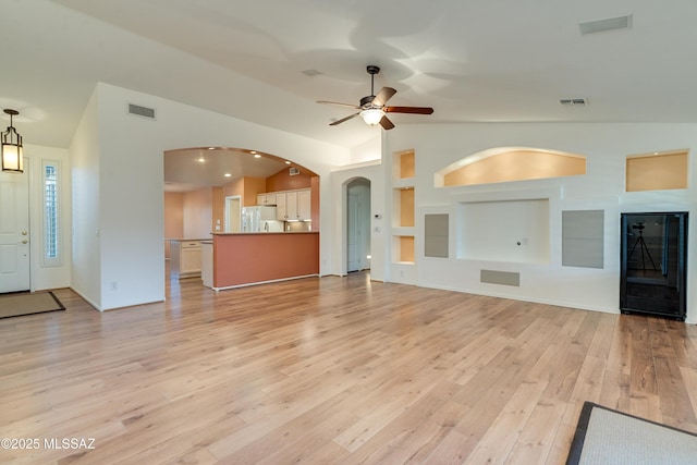 unfurnished living room featuring light wood-style flooring, vaulted ceiling, visible vents, and arched walkways