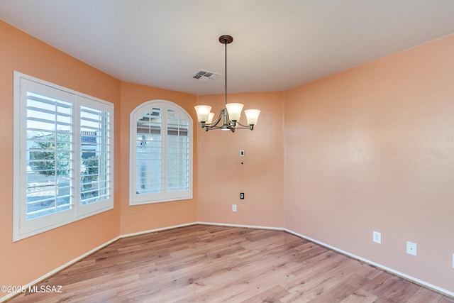 empty room featuring a chandelier, light wood-type flooring, visible vents, and baseboards