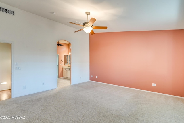 empty room featuring arched walkways, visible vents, a ceiling fan, light carpet, and vaulted ceiling