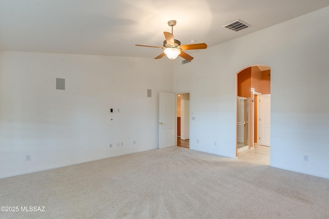 spare room with arched walkways, light colored carpet, visible vents, a high ceiling, and a ceiling fan