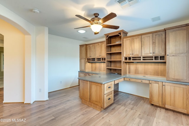 unfurnished office with visible vents, arched walkways, a ceiling fan, light wood-style flooring, and built in desk