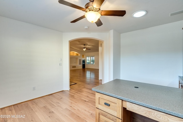 interior space with baseboards, arched walkways, a ceiling fan, light brown cabinetry, and light wood-style floors