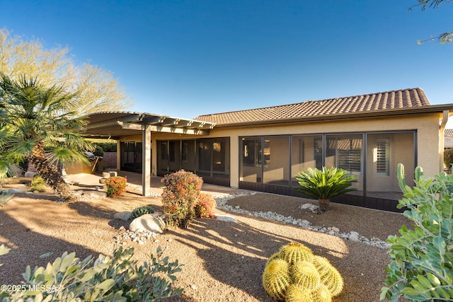 rear view of property featuring a sunroom, a tiled roof, stucco siding, a pergola, and a patio area