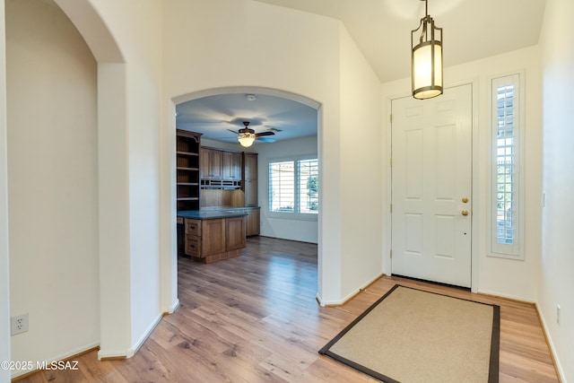 entrance foyer with light wood-style floors, arched walkways, ceiling fan, and baseboards